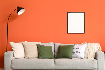 Comfortable grey sofa with soft pillows and floor lamp near orange wall in living room, closeup
