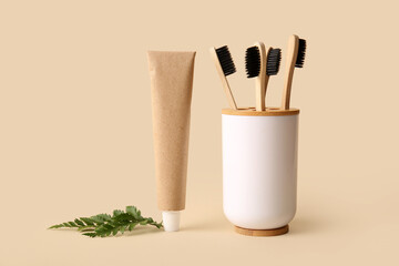 Holder with bamboo toothbrushes, leaves and tube of paste on beige background