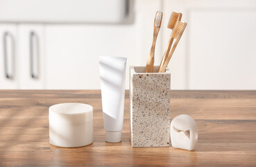 Holder with bamboo toothbrushes, dental floss and tube of paste on table in bathroom