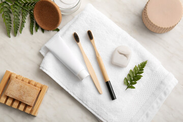 Bamboo toothbrushes with tube of paste, dental floss, soap bar and leaves on white background
