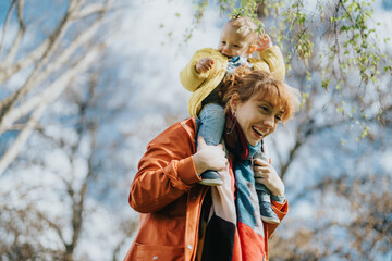 Joyful mother enjoys quality time bonding with her young child outdoors in nature. The parent carries the child, fostering closeness and fun, while surrounded by an uplifting and natural environment.