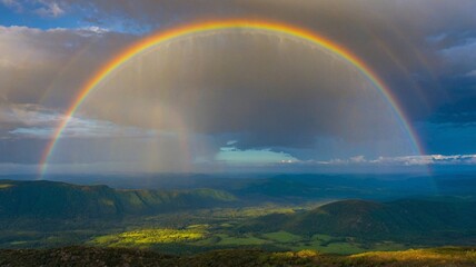Naklejka premium A stunning rainbow arches over a lush landscape, showcasing vibrant colors and a serene atmosphere after a rain shower.