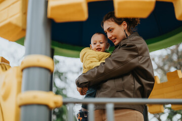 Obraz premium A loving mother tenderly carries her baby on vibrant playground equipment during a beautiful day.