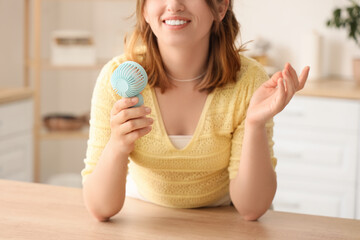 Young woman with mini fan in kitchen, closeup