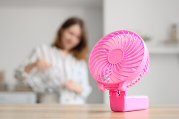 Mini fan on table against woman pouring water in kitchen, closeup