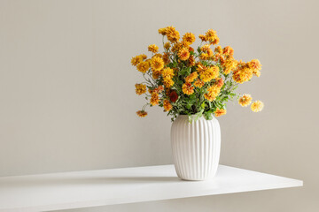 Bouquet of autumn yellow and orange flowers in white vase in sunny shadow on white surface. Minimal modern composition. Home interior and season decoration.