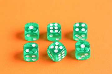 Green game dices on orange background, closeup