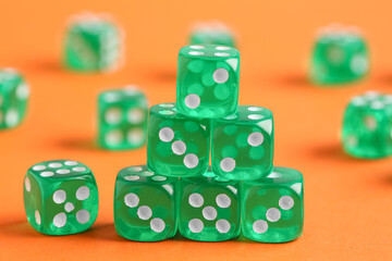 Green game dices on orange background, closeup