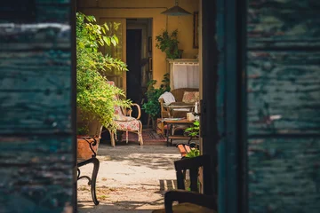 Fotobehang Mediterraans Europa Rustic Italian patio with vintage furniture, plants and cozy atmosphere, captured through open wooden doors. Warm light, intimate mood, Mediterranean style.  © Aga Bak