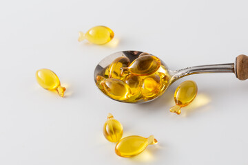 Fish-shaped Softgels on Spoon with Oil Drops Isolated on White Background