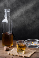 Glass of amber liquor beside bottle and ashtray on wooden table