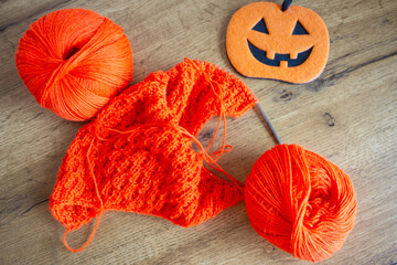 Orange wool and knitting needles with decorative pumpkin. Halloween still life. Cozy lifestyle...
