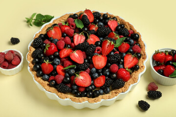 Sweet tart with different fresh berries and mint on yellow background