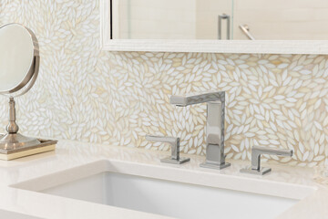 A bathroom faucet detail with a chrome faucet on a marble countertop with a mosaic leaf pattern...