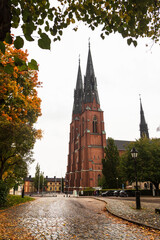 Fototapeta premium Uppsala, Sweden - 2 October 2022: Uppsala Cathedral with yellow leaves around in autumn 