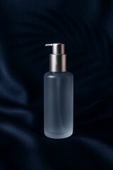 Frosted cosmetic pump bottle with silver collar on navy silk background, elegant skincare packaging mockup.