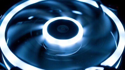 A spinning computer case fan with bright blue LED illumination in a dark environment, creating motion blur.