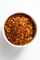 Red chili flakes in white bowl on a bright background, top view