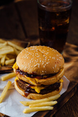 Juicy double cheeseburger with fries and soft drink on wooden table