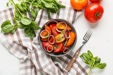 Bowl of fresh tomato salad with red onion and basil leaves on white background