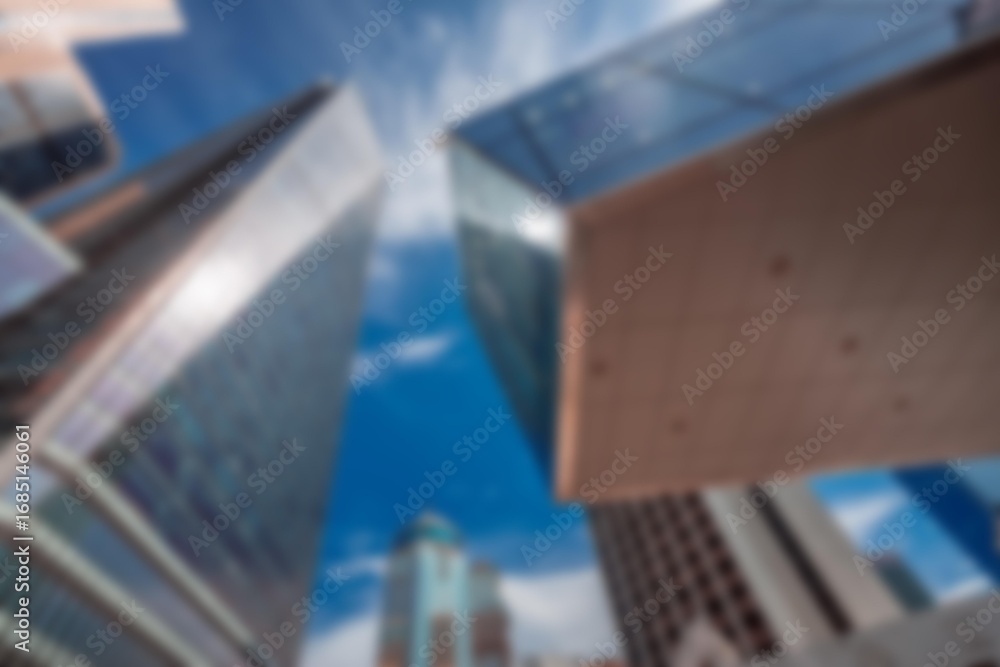 Poster an abstract blur of tall buildings against a clear blue sky with white clouds. the sky is in focus a
