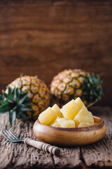 Fresh Cut Pineapple Slices in Wooden Bowl with Whole Fruits Background