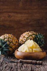Fresh Pineapples and Sliced Pineapple in Wooden Bowl on Rustic Table