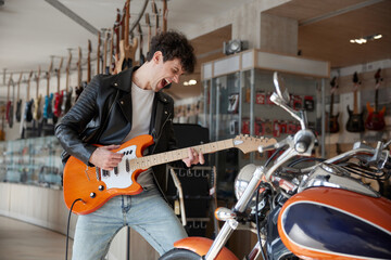 Expressive man in a leather jacket is playing guitar in a store