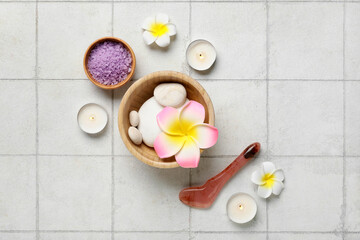 Obraz na płótnie Canvas Burning candles, bowls with spa stones, plumeria flowers and sea salt on beige tile background