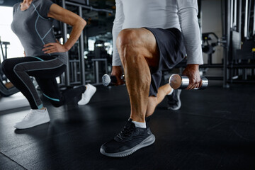 Mature man and a woman squatting with dumbbells inside a gym