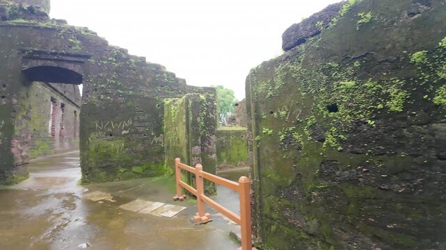 Detailed interior view of weathered laterite stone walls covered in green moss and damaged medieval architecture inside the ruins of St. Augustine Church in Old Goa, India.