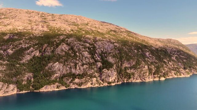 Rugged mountain slope with rocky cliffs and green forest descends to turquoise waters at Ombaksbotn