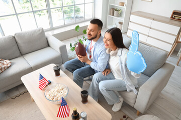 Young couple with USA flags watching rugby game at home