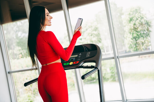 Fitness trainer in vibrant red activewear using smartphone on treadmill in a bright gym setting, embracing fitness - Powered by Adobe