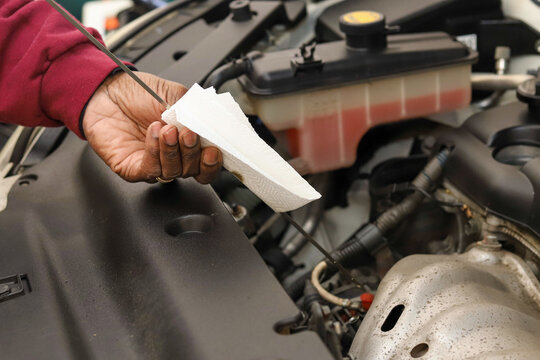 A close-up of a black man checking   oil in a car with a dipstick