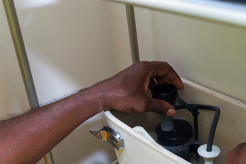 A black man repairing a toilet