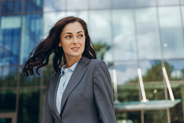 Fototapeta premium Businesswoman smiling and looking away with hair blowing in wind in front of office building