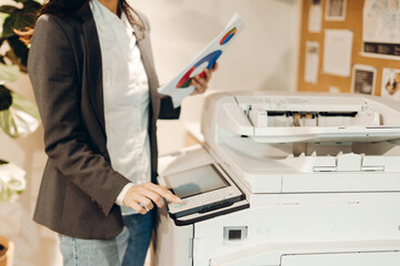 Businesswoman using office printer while holding charts and graphs