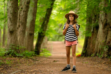 Young girl with a backpack walks forward on a forest path, observing her surroundings with wonder....