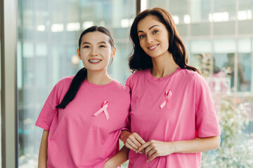 Two smiling women wearing pink ribbon showing support for breast cancer awareness