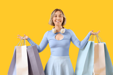 Beautiful woman with shopping bags on yellow background