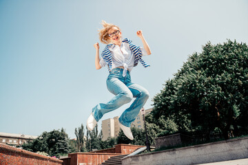 Young woman jumping outdoors in a casual outfit during a sunny day, expressing joy and carefree...