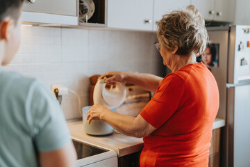 An elderly grandmother in a vibrant red shirt instructing a young child in kitchen activities,...