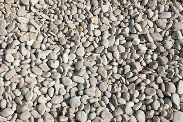 Beige and ivory pebbles spread across the shore, illuminated by sunlight, creating a soothing texture perfect for backgrounds, spa concepts, or seaside projects.