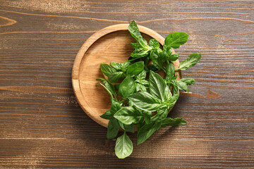 Plate with fresh green basil leaves on wooden background