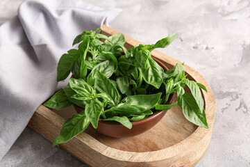 Bowl with fresh green basil leaves on grey background, closeup