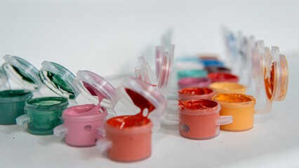 Open acrylic paint containers with green, pink and red colors in focus, artistic supplies close-up
