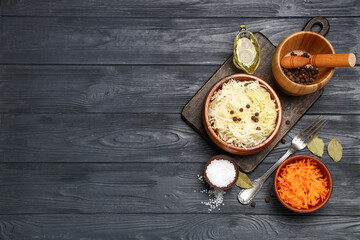 Bowl with tasty sauerkraut and different ingredients on black wooden background