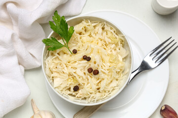 Bowl with tasty sauerkraut, parsley and peppercorns on white background