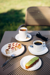 Pistachio eclair, cake slice, and coffee on a table in garden terrace setting.